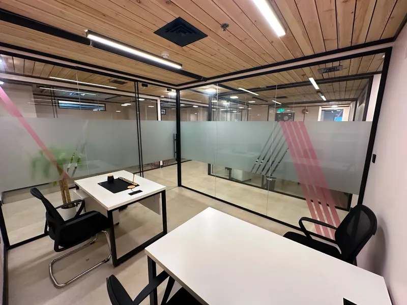 Office 23 · two desks in The Collective, inside frosted glass walls with pink stripes under a wood-slat ceiling
