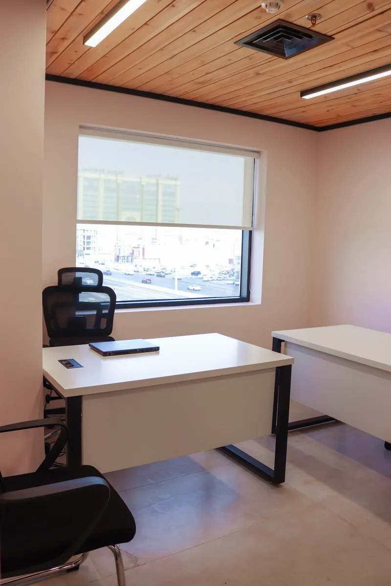Office 37 · desk in front of a window with a roller blind, a second desk on the right