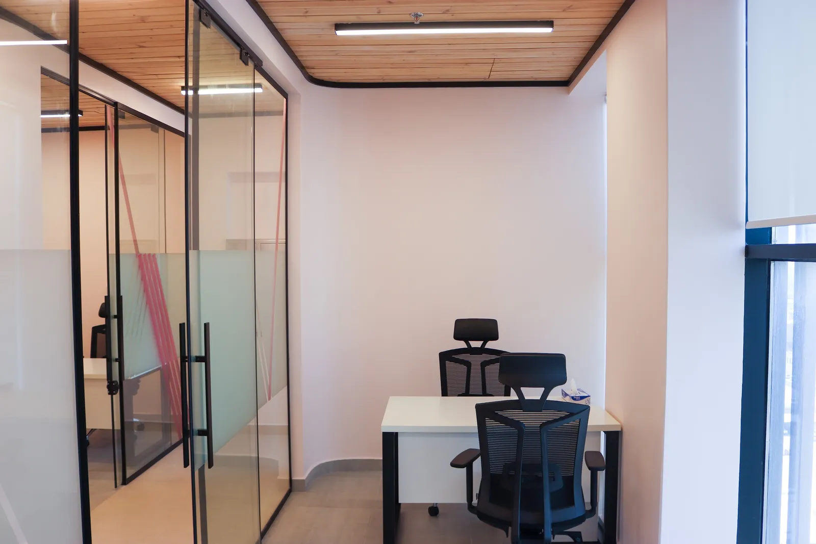 Office 70 · desk with two mesh chairs, glass sliding doors and a timber-slat ceiling
