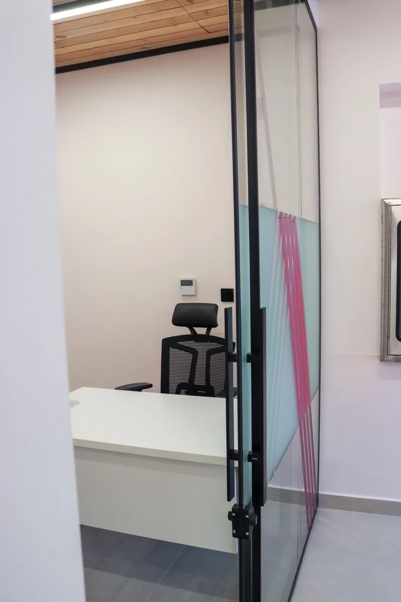 Office 69 · desk and high-back mesh chair seen through the glass door, timber-slat ceiling above