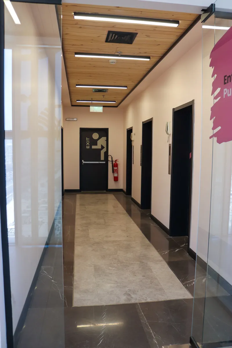 14th floor · lift lobby with three lifts, marble floor and a timber ceiling, seen through the glass entrance