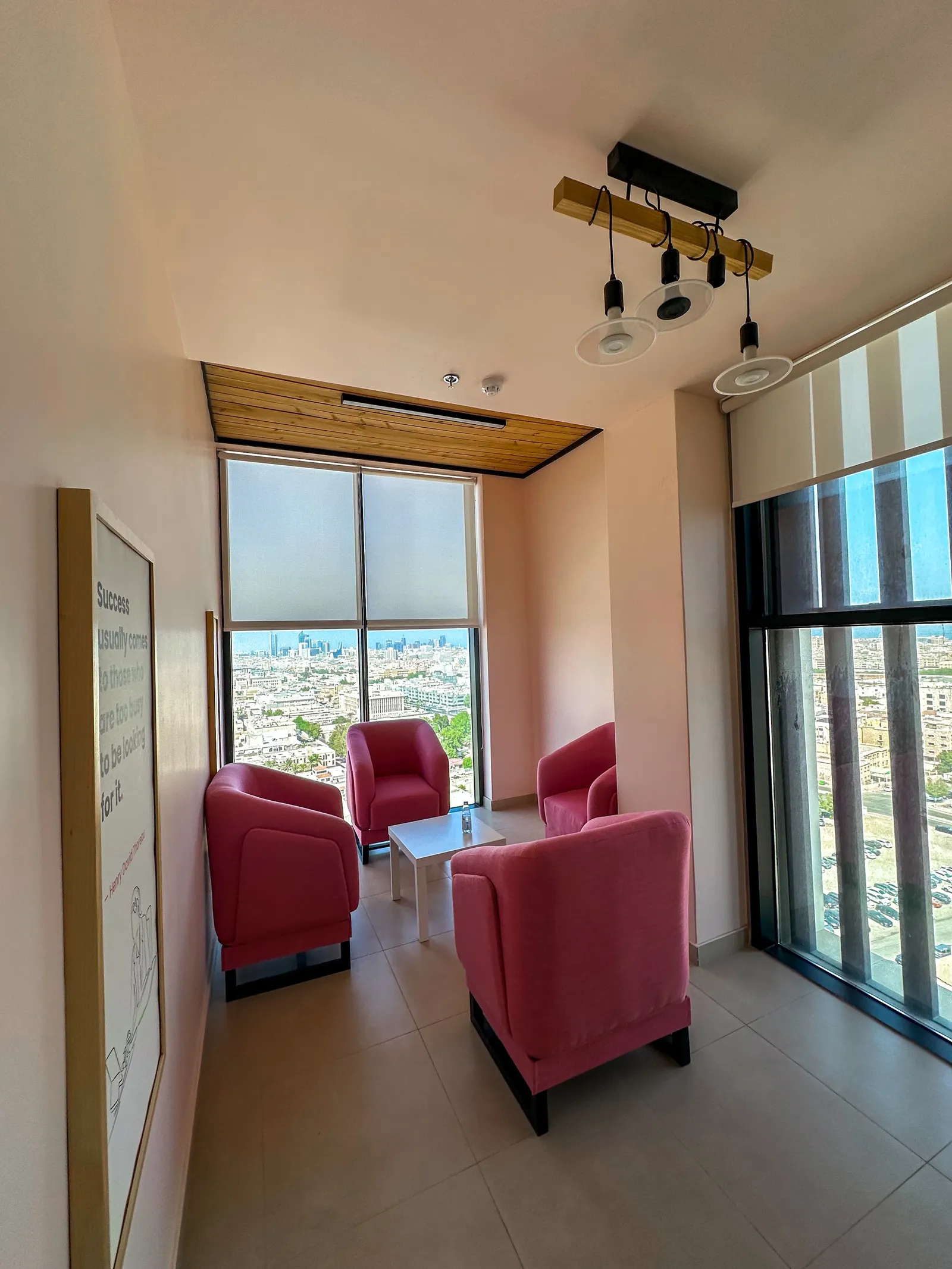 Sky Bridge · pink armchairs round a low table, wood-beam pendant and city-view windows