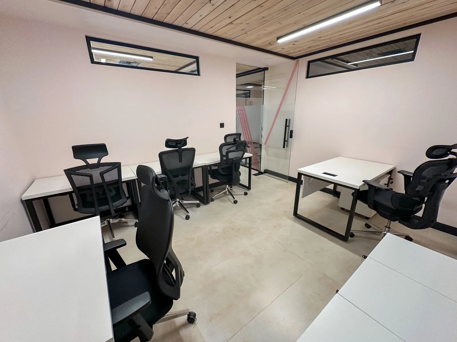 Office 25 · rows of desks with high-back mesh chairs under a pine-slat ceiling, with a glass door