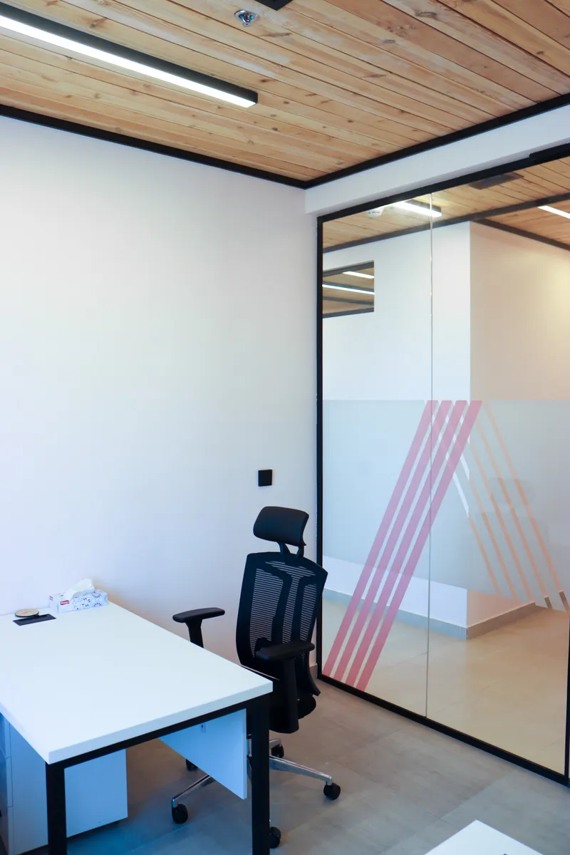 Office 66 · desk and ergonomic chair beside the glass wall with pink-striped frosting