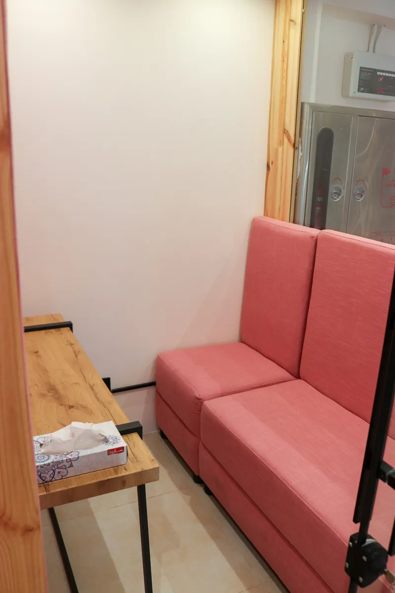 Pink two-seat sofa and a wooden shelf desk inside a glass-walled pod