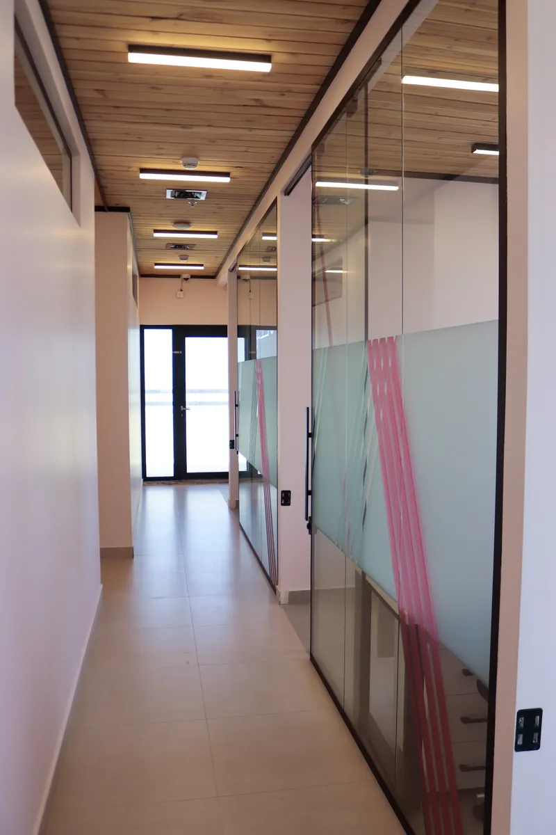 14th floor · corridor past glass office fronts with frosted bands and pink stripes, ending at a glazed door