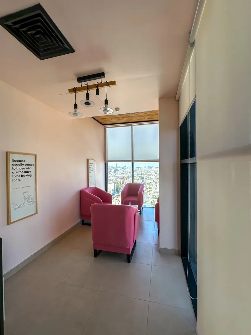 Sky Bridge · pink armchairs under a wood-beam pendant facing a window over the city