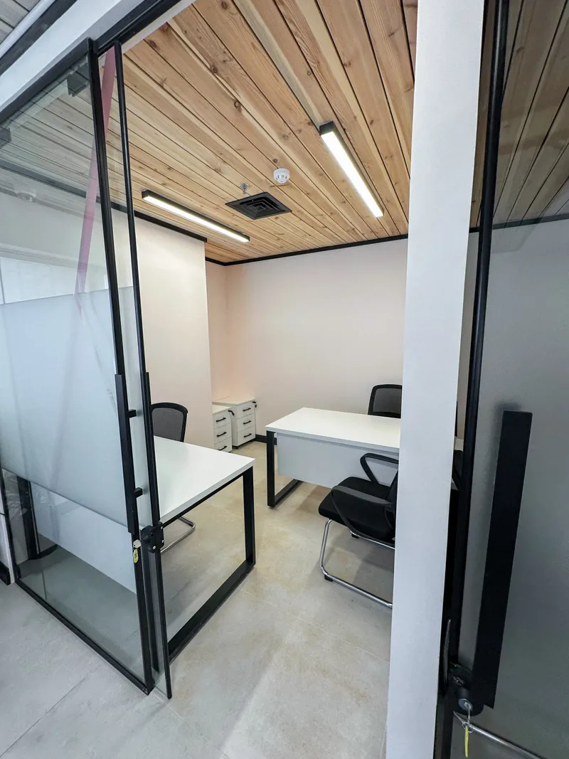 Office 35 · two desks and drawer pedestals under a wooden ceiling, seen through the open glass door