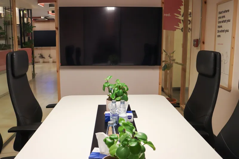 White meeting table set with plants and water, black leather chairs and a wall screen