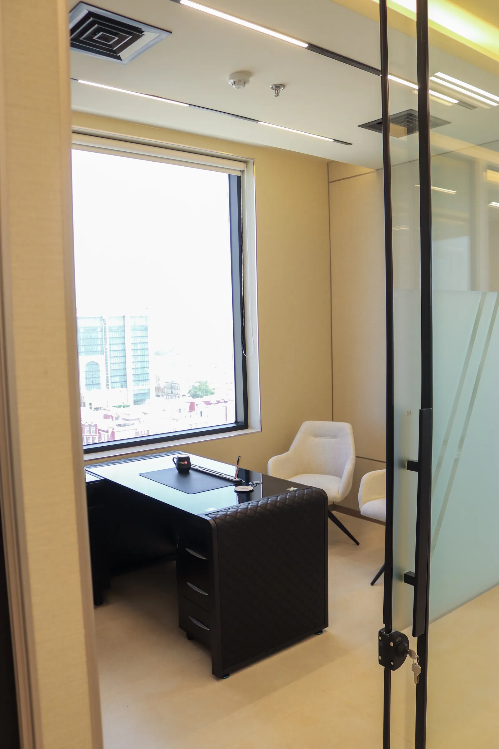 Office 54 · desk, two guest armchairs and a city-view window seen through the glass door