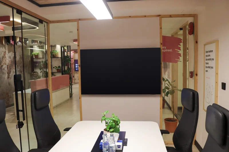 Meeting table with black leather chairs facing a wall screen, glass walls onto the reception beyond