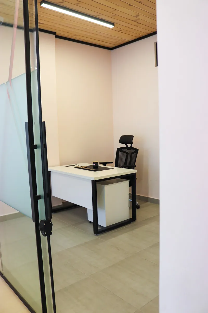 Office 68 · desk and high-back mesh chair seen through the glass door, timber-slat ceiling above