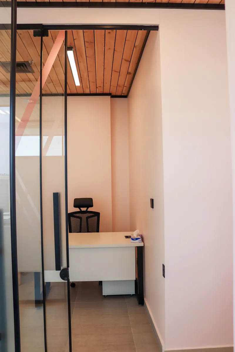 Office 67 · desk and high-back mesh chair seen through the glass door, under a timber-slat ceiling
