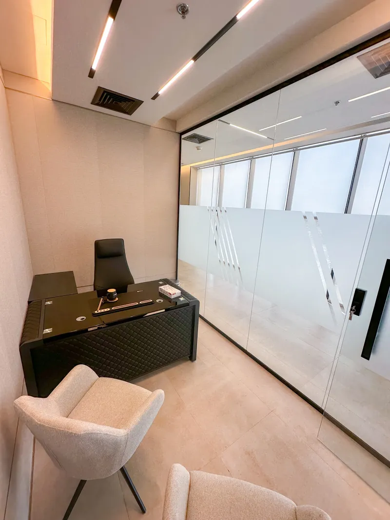 Office 62 · desk, guest armchairs and glass wall facing a window-lined corridor