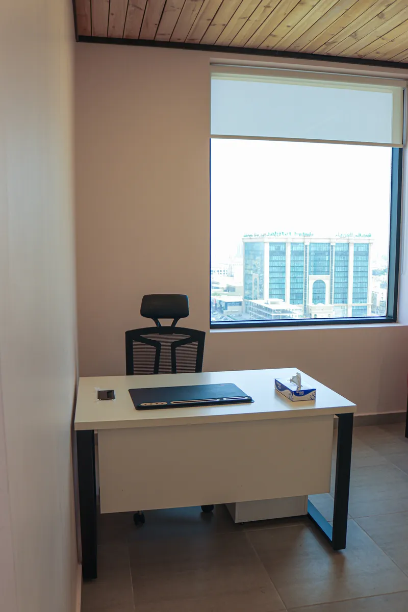 Office 66 · desk and mesh task chair under a timber ceiling, city view beyond