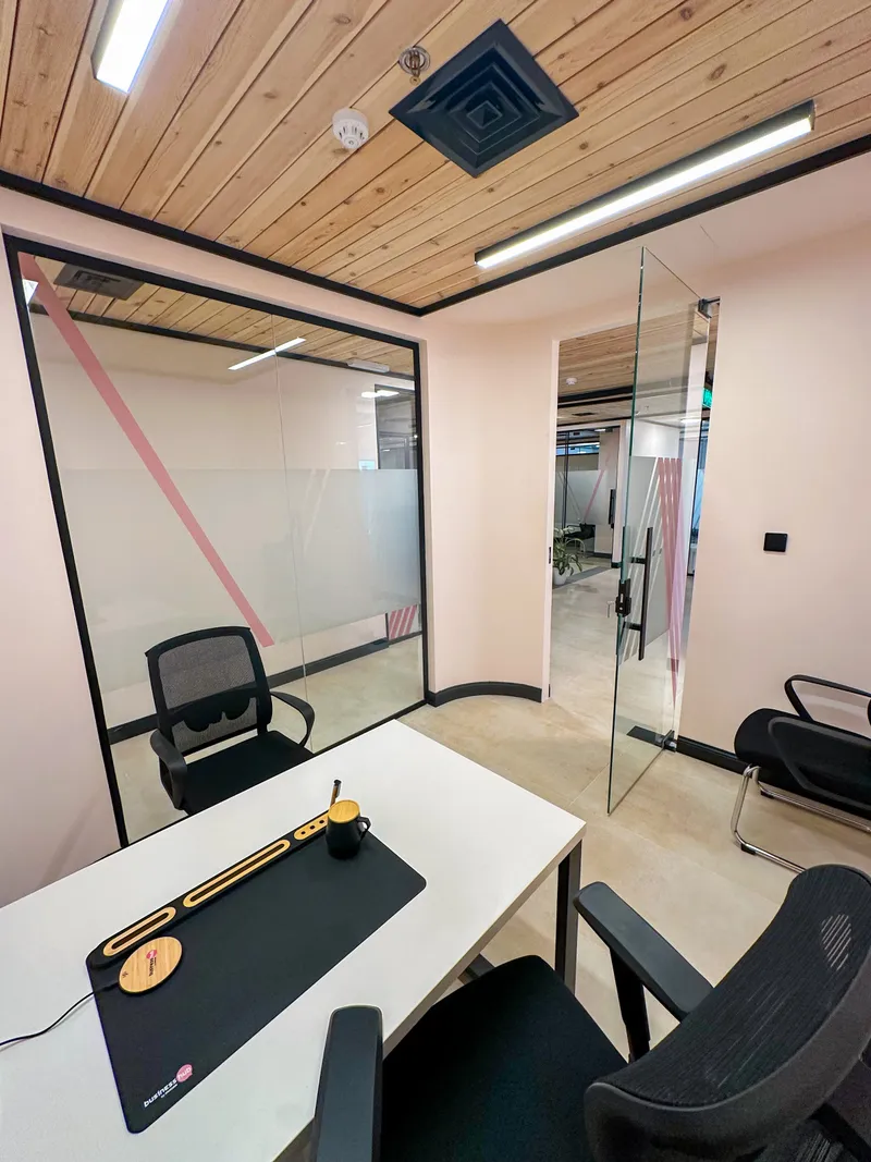 Office 32 · desk facing a glass partition with pink stripes and an open glass door to the corridor