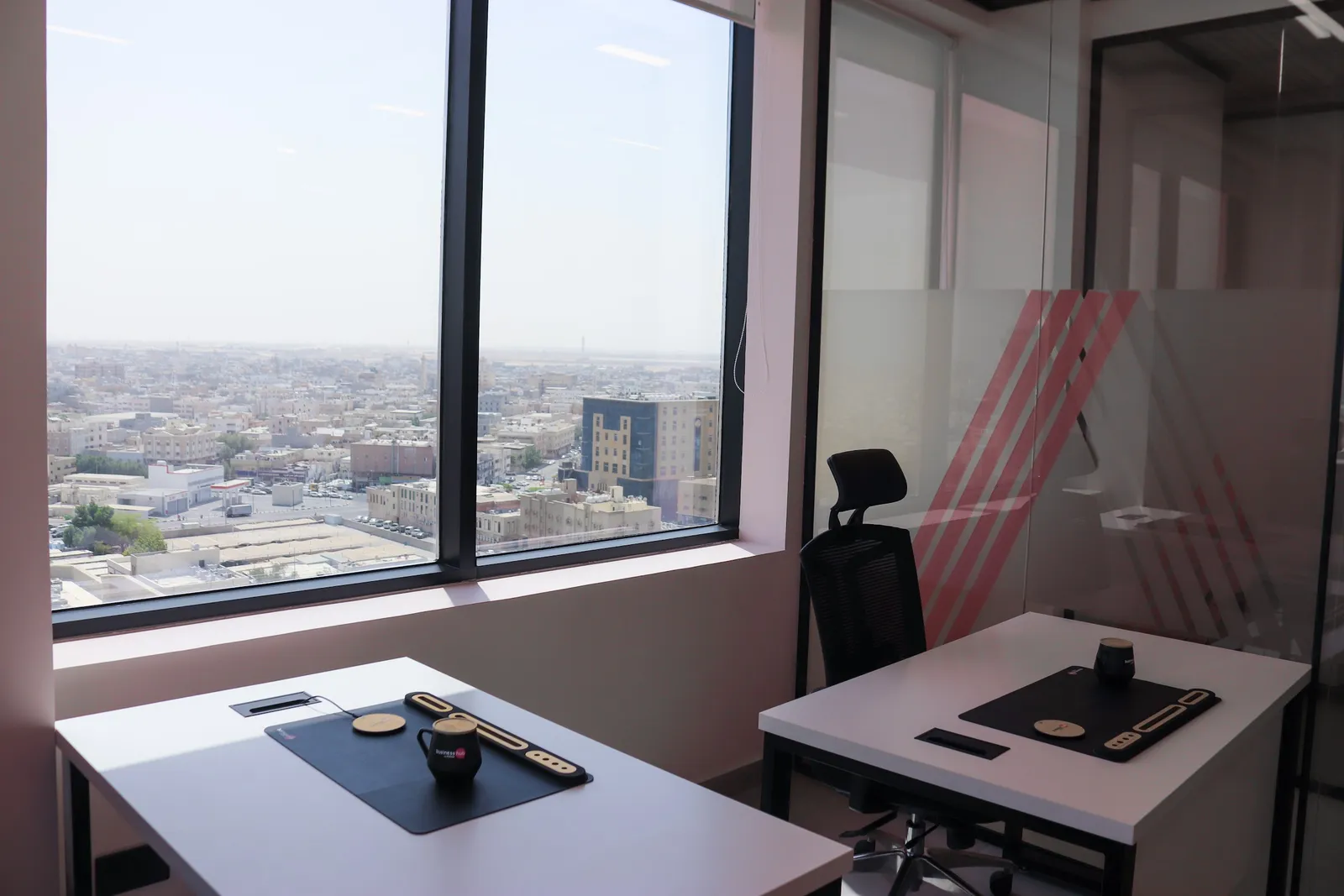 Office 64 · two desks at a corner window over the city, beside a frosted glass partition