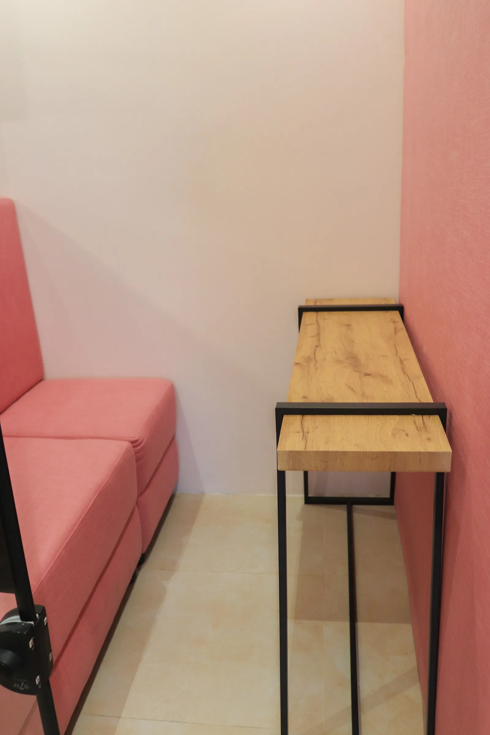 Wooden shelf desk beside a pink sofa in a two-seat pod