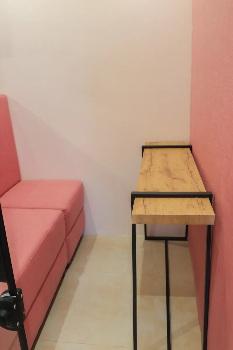 Wooden shelf desk beside a pink sofa in a two-seat pod