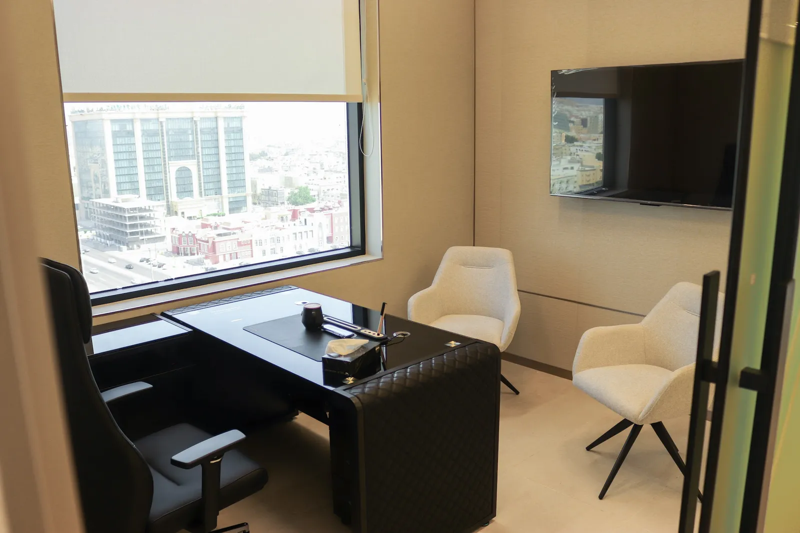 Office 56 · desk, two guest armchairs, wall-mounted TV and a city-view window