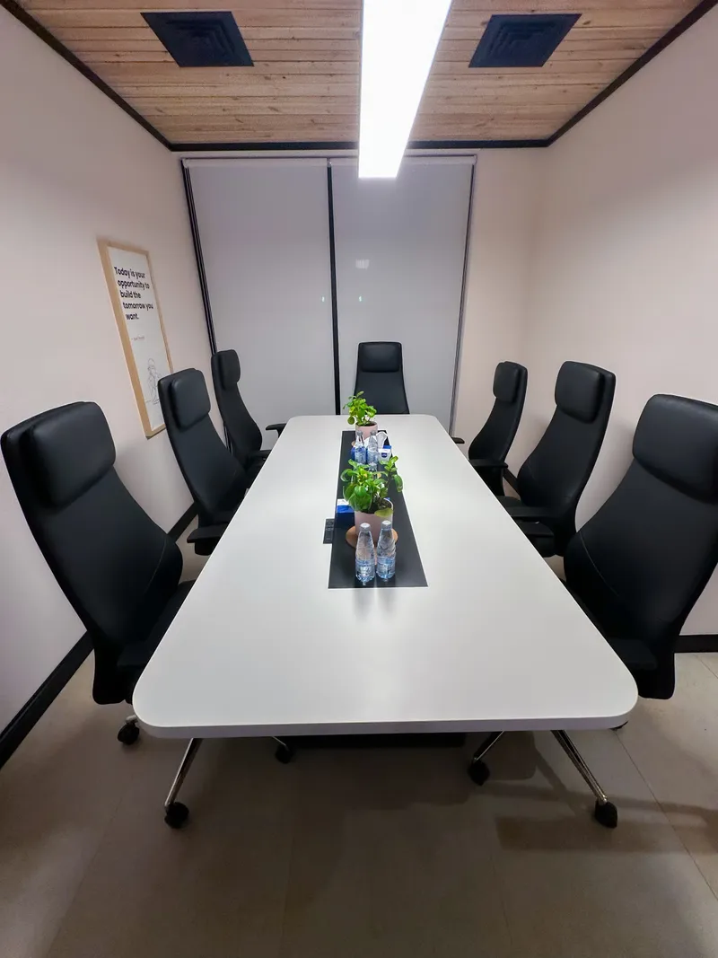 Seven black chairs around a white meeting table under a timber ceiling