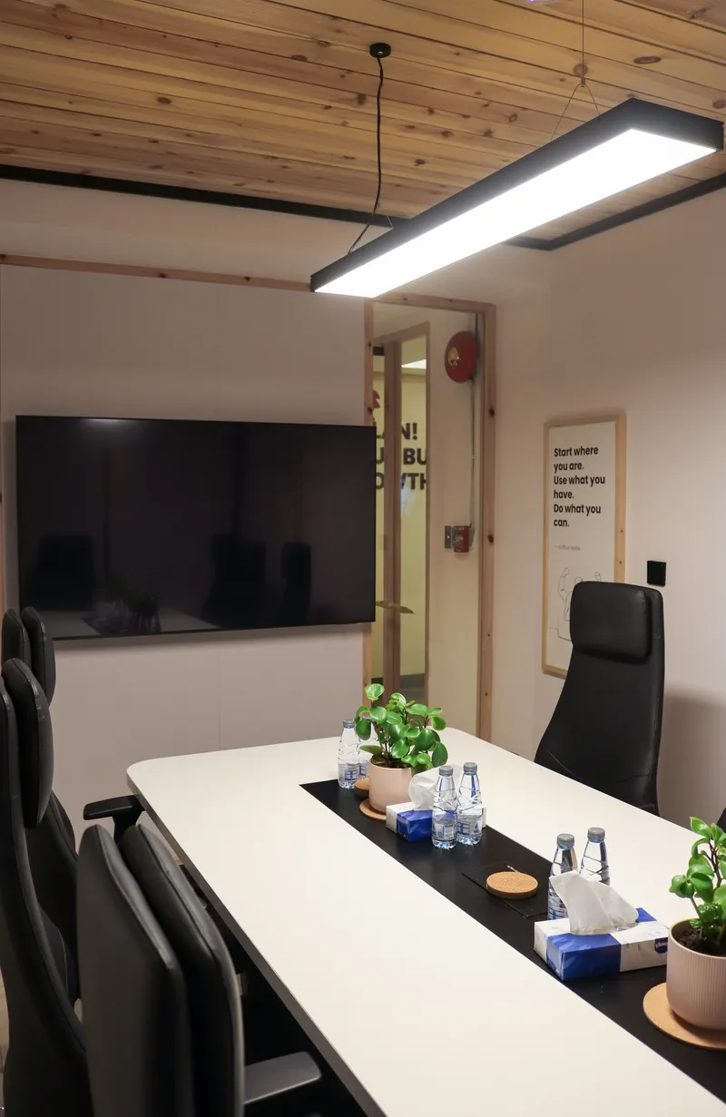 Meeting table under a pendant light, with a wall screen and a framed quote print