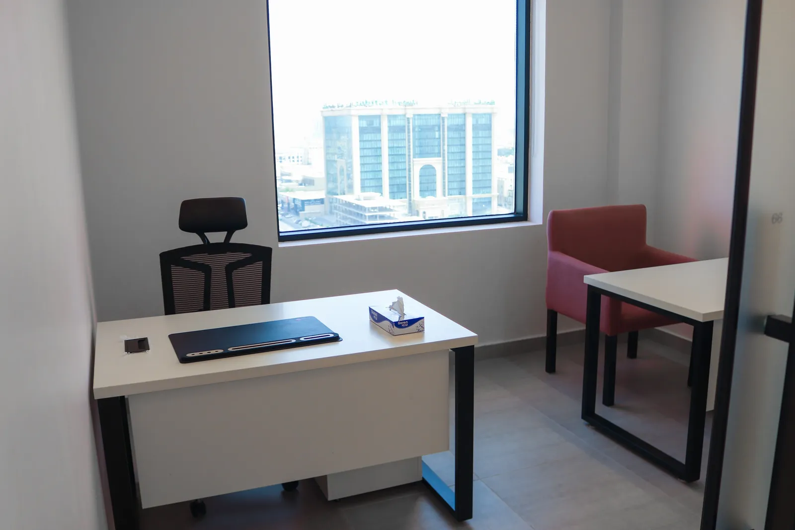 Office 66 · desk, task chair and pink armchair by a large window over the city